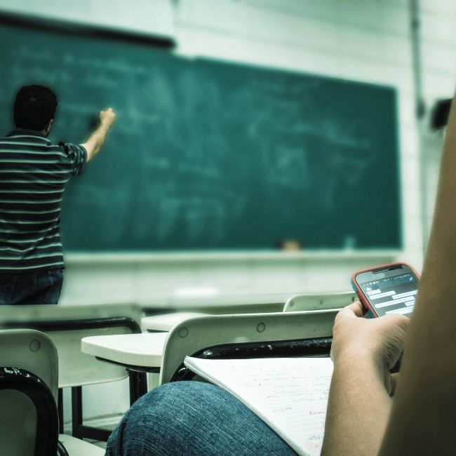 aluno a escrever no quadro de giz. aluno com smartphone na mão a consultar conteúdos. ambiente de escola de formação.